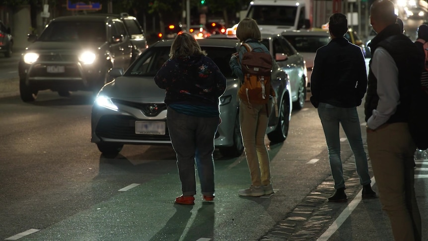 People watch passing cars on a dark street outside Melbourne Park