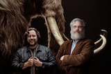 Colossal co founders Ben Lamm and George Church pose in front of woolly mammoth tusks. 
