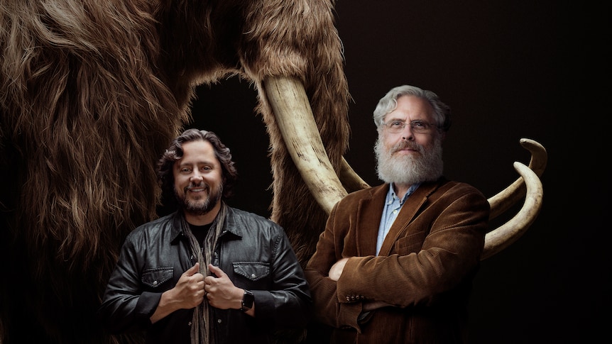 Colossal co founders Ben Lamm and George Church pose in front of woolly mammoth tusks. 