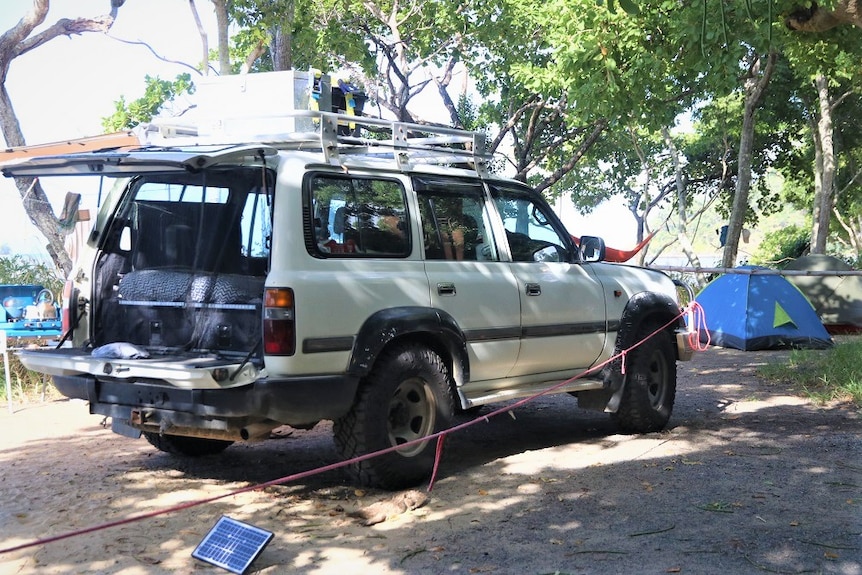 Four wheel drive with boot open and red rope attached to bull-bar, with blue and green tent in background.