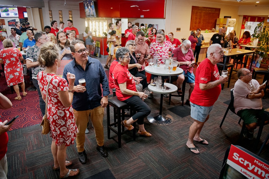 A crowd of people, many wearing red and with a drink in hand, gathered in a pub-type room.