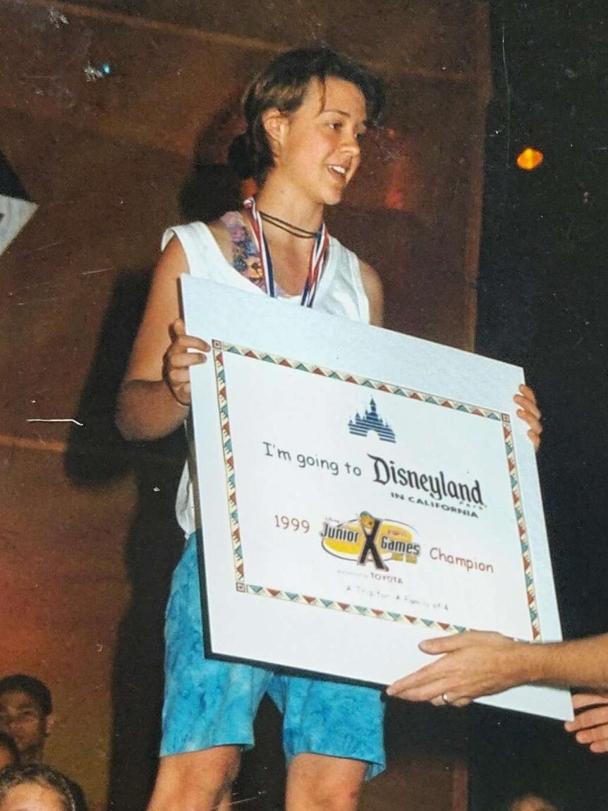 A girl is handed a large certificate which says "I'm going to Disneyland".