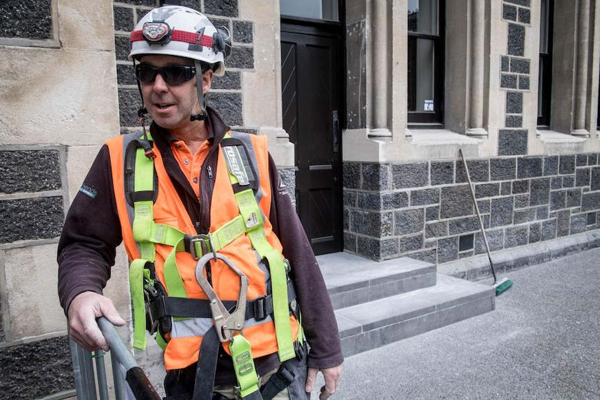 A stonemason in high-vis gear leans against a stone wall