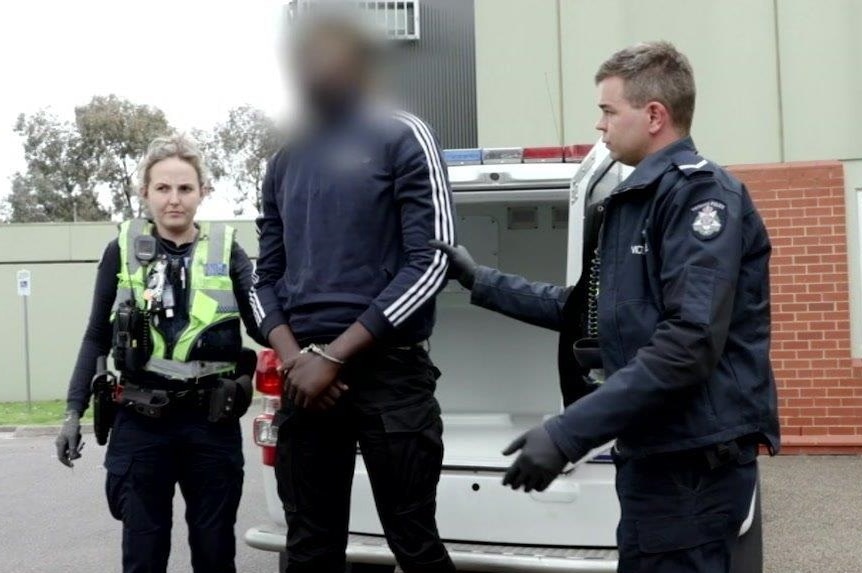 A man stands handcuffed with a police officer standing either side of him.