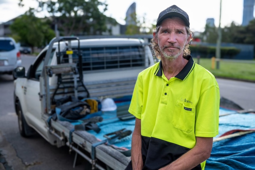 David in a high vis work shirt leans against a ute.