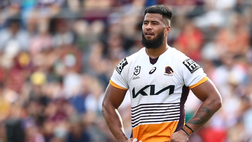 A Brisbane Broncos NRL player stands with hands on his hips, holding his mouthguard as he looks downfield.