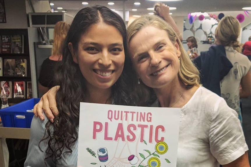 Two women smile as they hold a poster promoting their book Quitting Plastic.