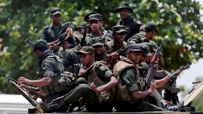 Sri Lankan soldiers holding guns sit on the top of a military vehicle.