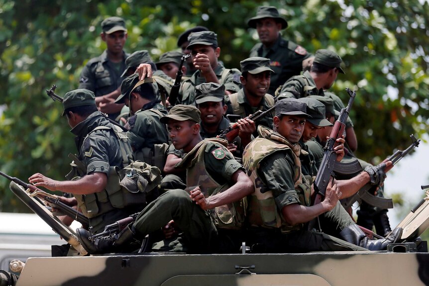 Sri Lankan soldiers holding guns sit on the top of a military vehicle.