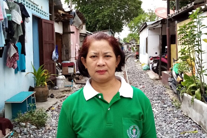 A woman wearing a green shirt stands in a street in Thailand.