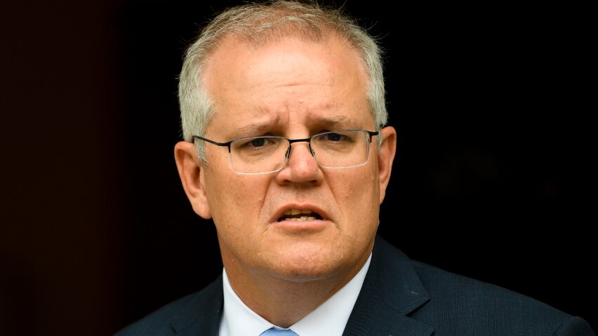 Scott Morrison in a suit infront of an australian flag looking at the camera