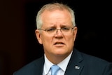 Scott Morrison in a suit infront of an australian flag looking at the camera