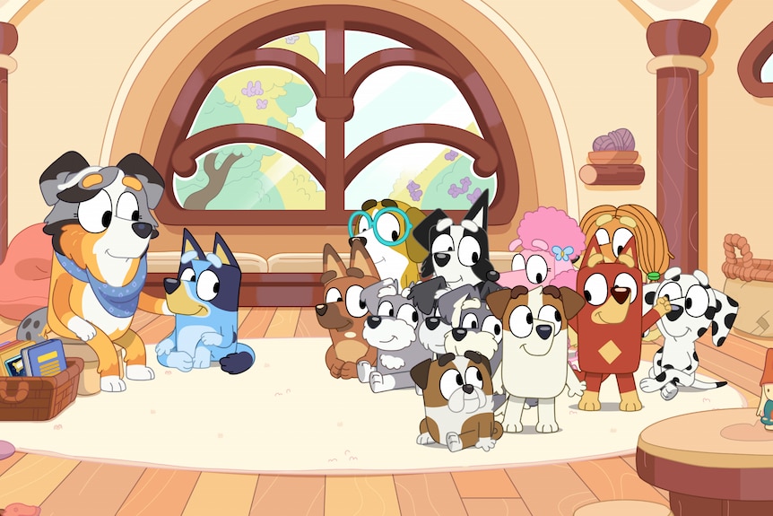 A still from Bluey in the classroom. Bluey sits close to their teacher Calypso, the rest of the students sit behind her