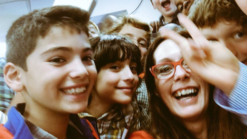 A selfie with a woman smiling widely at the centre, and laughing and smiling young students crammed in close to her.