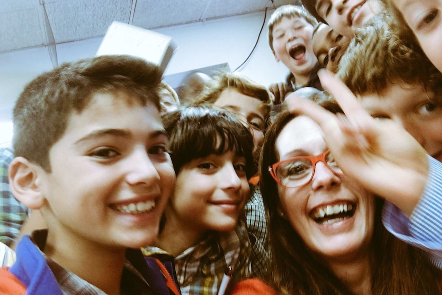 A selfie with a woman smiling widely at the centre, and laughing and smiling young students crammed in close to her.