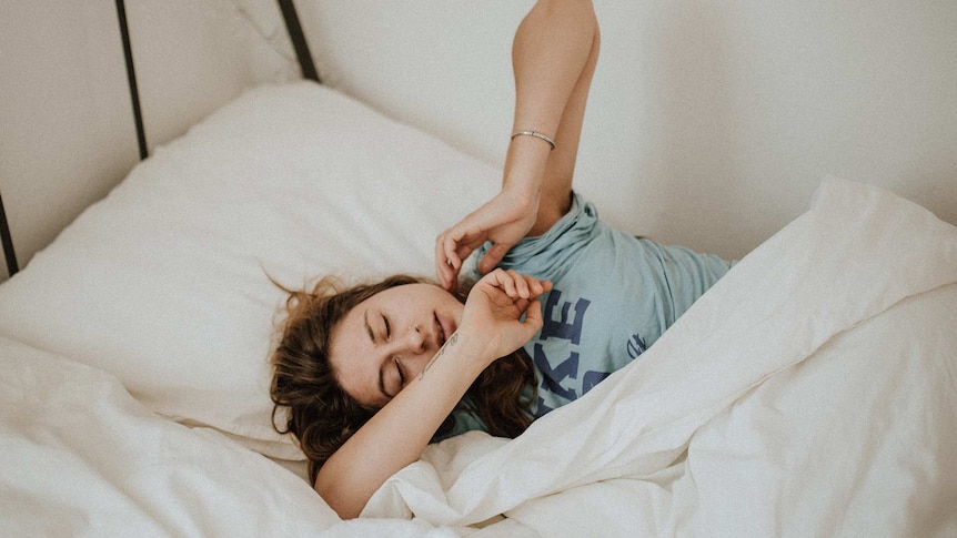 woman sleeping on white bed while trying to get some sleep in a story about sleeping tips during coronavirus pandemic.