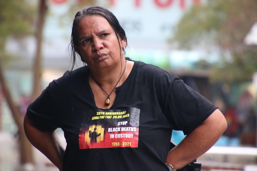 An Indigenous woman wearing a t-shirt that says 'stop black deaths in custody'. 