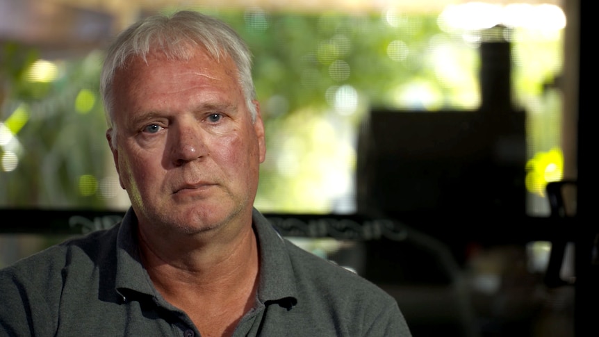 A middle-aged man looks into camera with a serious expression.