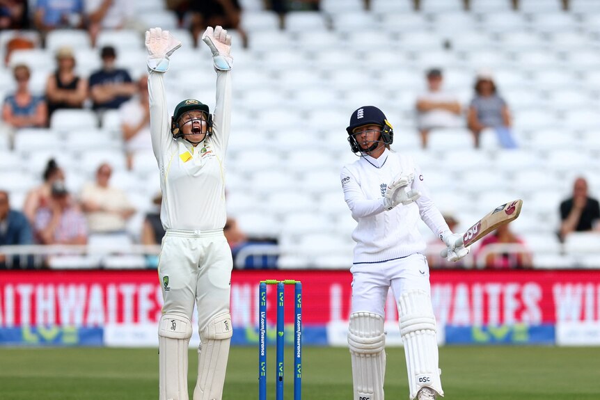 A players dressed in white raises their bat while a player with a bat looks concerned. 