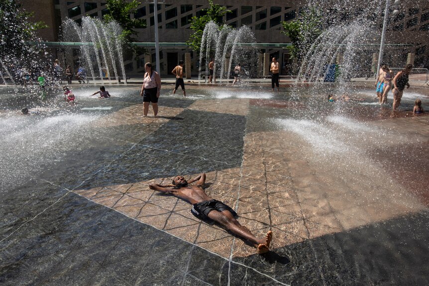 A man relaxes submerged on his back in a fountain as a heatwave grips Alberta, Canada.