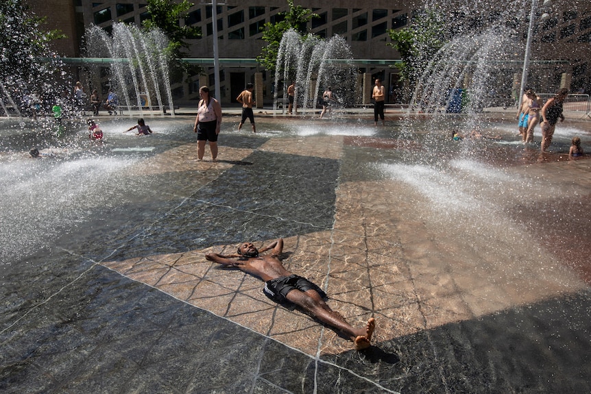 A man relaxes submerged on his back in a fountain as a heatwave grips Alberta, Canada.