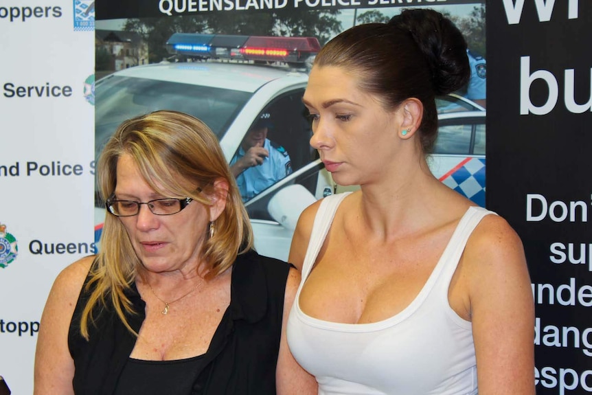 An older blonde woman and a younger, dark-haired woman speaking in front of a Queensland Police backdrop.