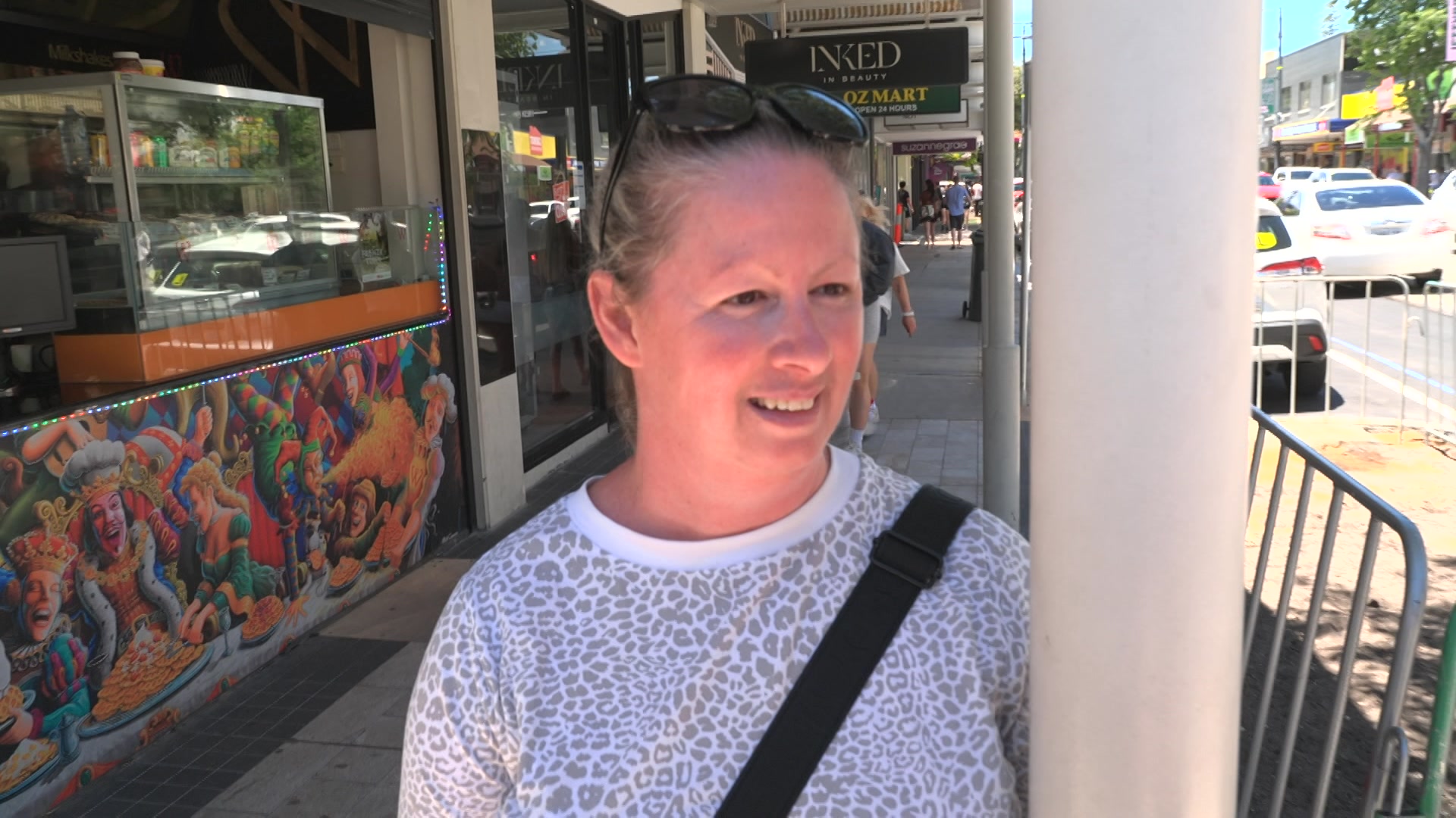 Uma mulher está parada na beira de uma rua. Ela está sorrindo.