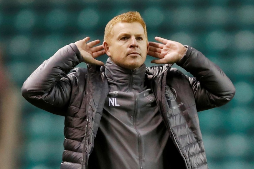 Neil Lennon cups his ears in his hands wearing a jacket