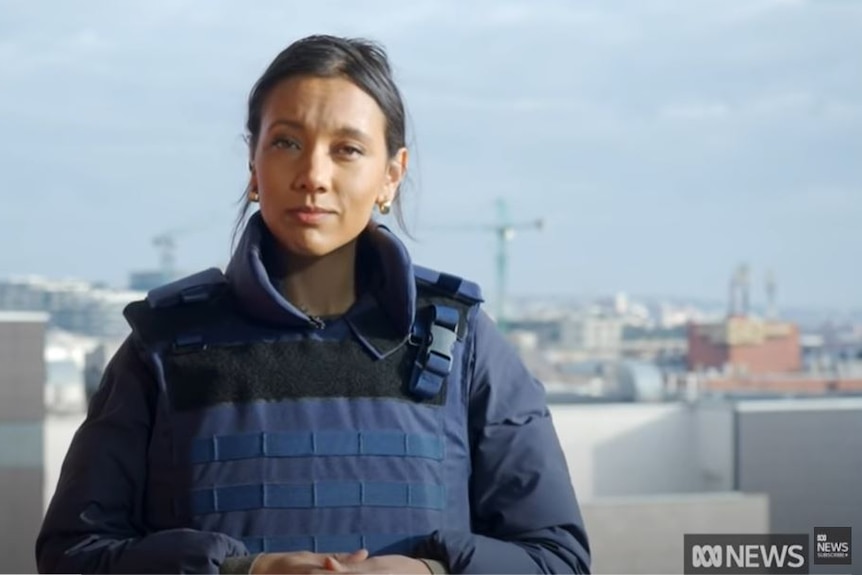 A woman wearing a blue protective vest speaks to camera