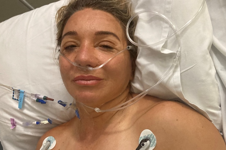 A woman looks at a camera from a hospital bed. 