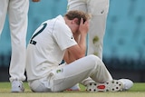Australia A players, wearing whites, surround Cameron Green, who is on the floor after being hit in the head by a cricket ball.