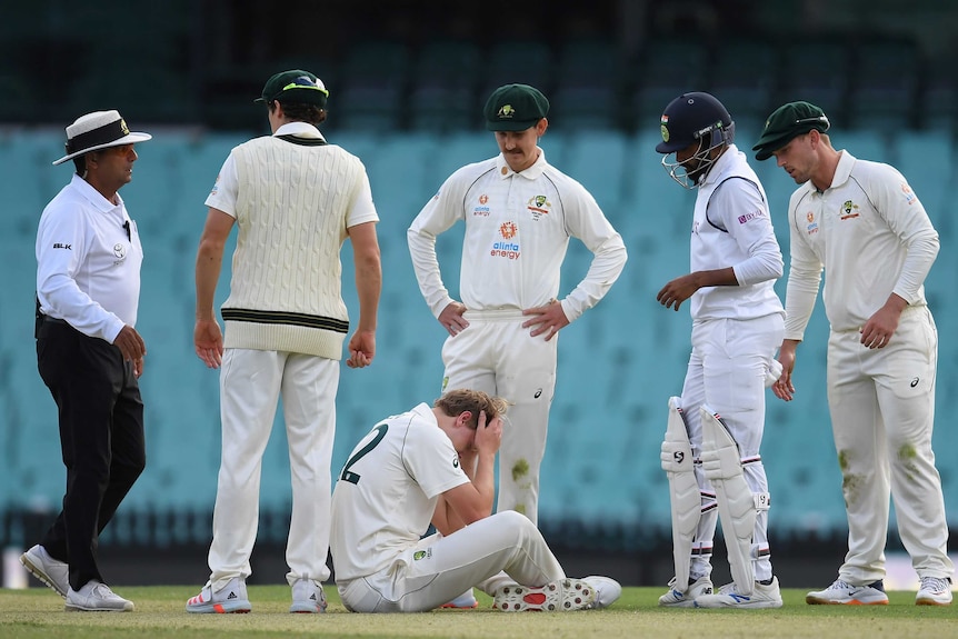 Australia A players, wearing whites, surround Cameron Green, who is on the floor after being hit in the head by a cricket ball.