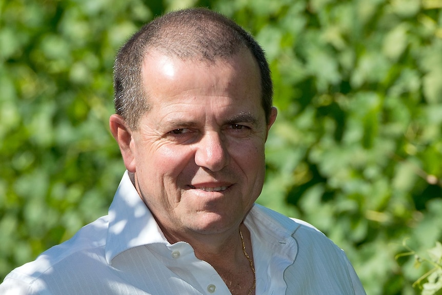 A man stands in a vineyard smiling at the camera.