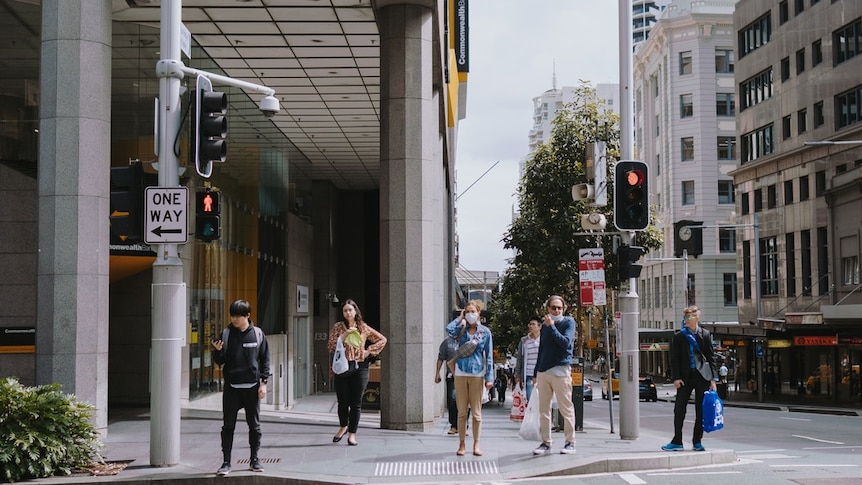 A group of people wait to cross the road in Sydney's CBD. Some are wearing masks.