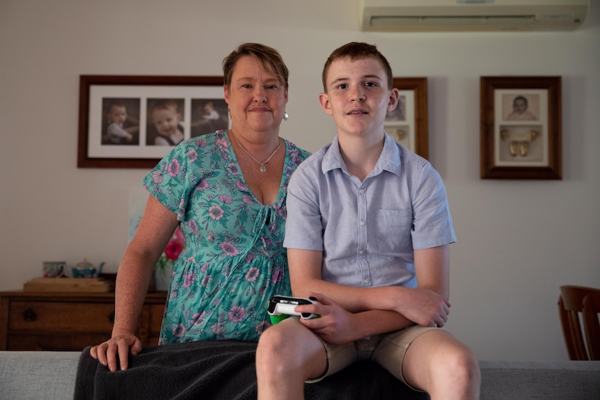 Mum standing next to teenage son who holds a gaming controller 