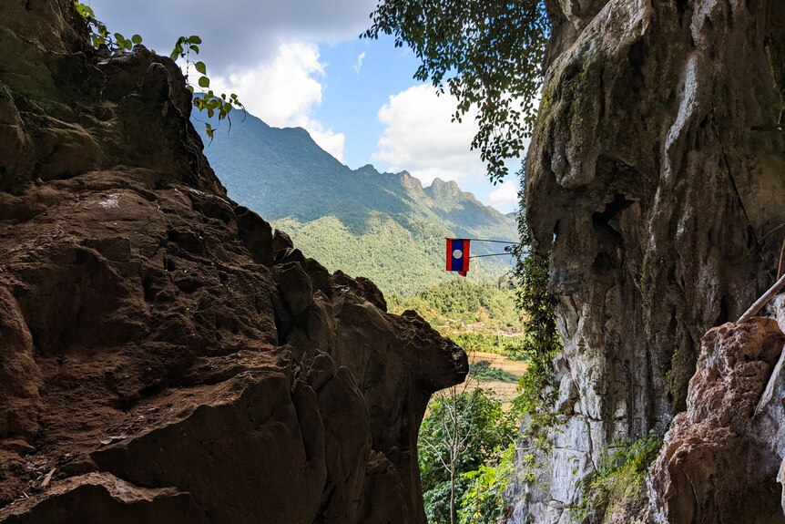 Green coverd mountains with a Laos flag hanging off a cliff face.