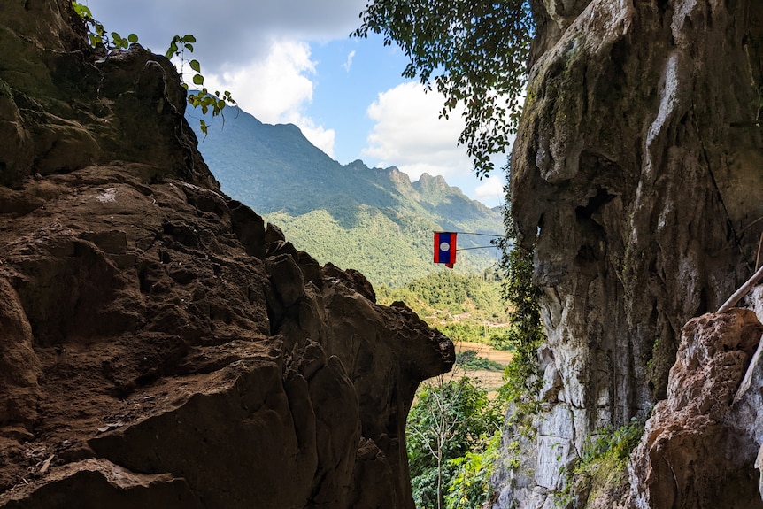 Green coverd mountains with a Laos flag hanging off a cliff face.