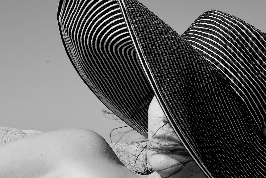A woman's face peeks from behind a large sun hat.