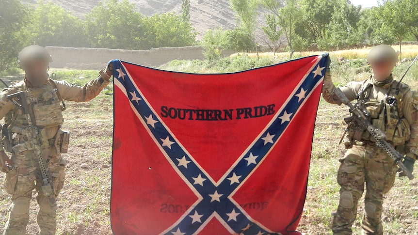 Two soldiers with faces blurred holding a flag.