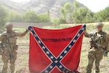 Two soldiers with faces blurred holding a flag.