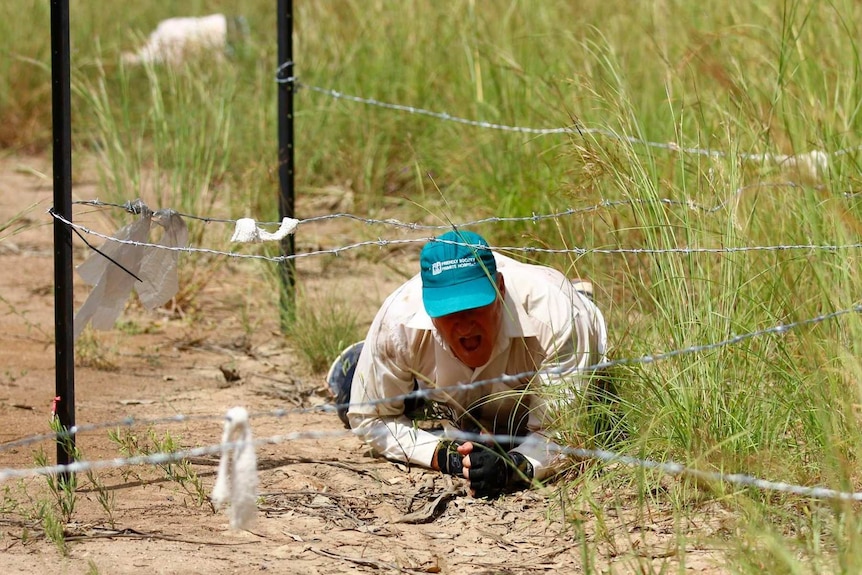 Dave Holleran crawls on his stomach underneath a series of barbed wire fences.