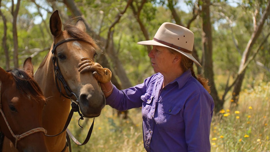 A horse trainer pats her horse's head.