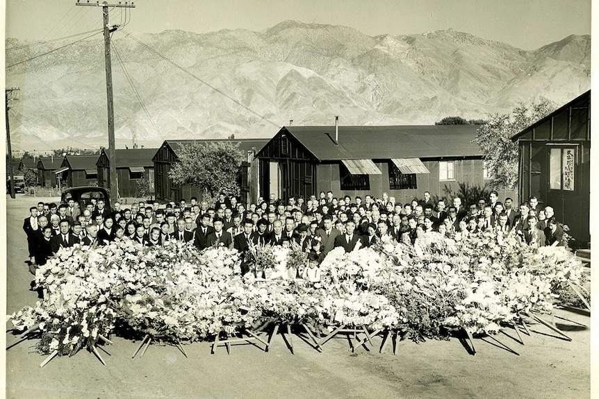 A black and white photo of a large gathering of people with flowers.
