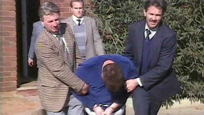 Police officers drag Craig Minogue to a police car.