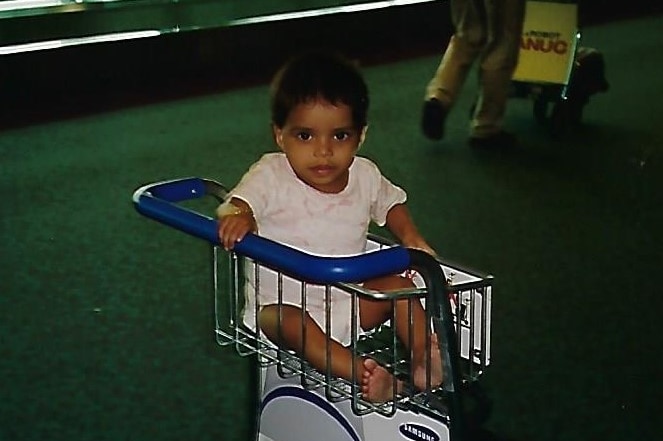 A baby sits in an airport baggage trolley