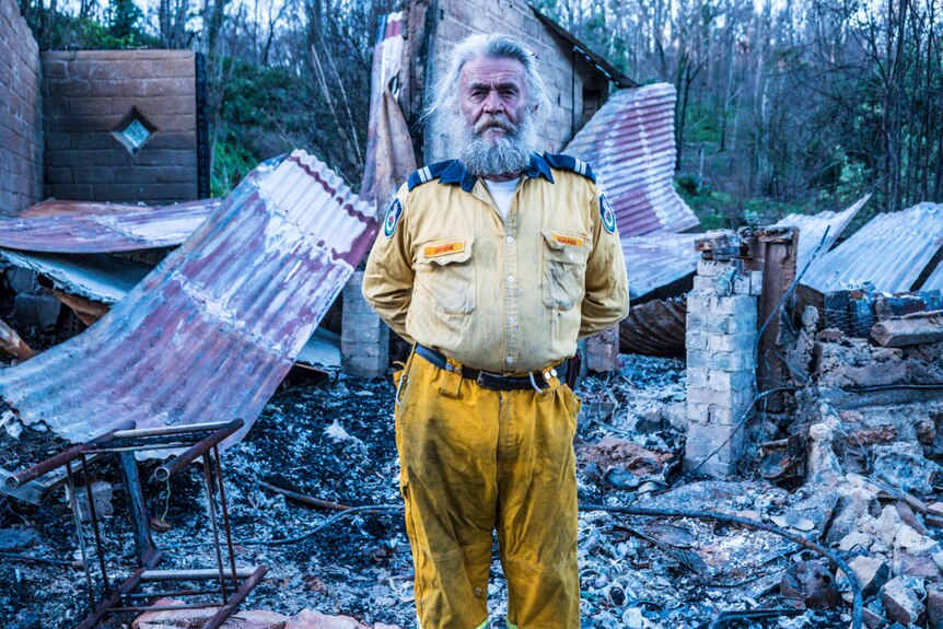 Bearded man in Rural Fire Service uniform standing in front of his burnt home