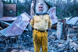 Bearded man in Rural Fire Service uniform standing in front of his burnt home