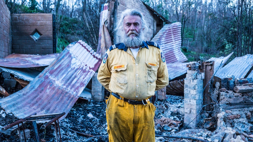 Bearded man in Rural Fire Service uniform standing in front of his burnt home