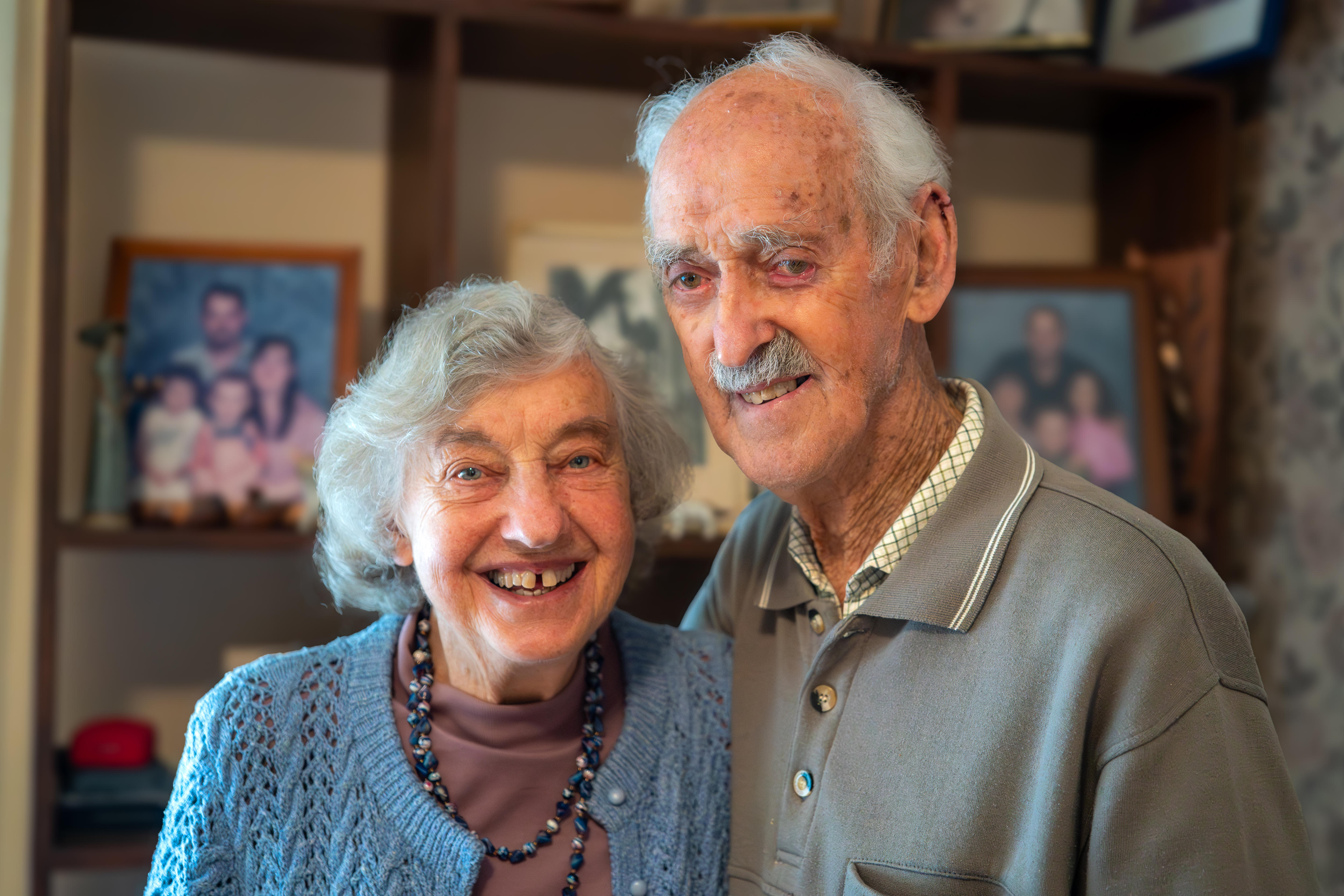 A woman and man smile, with family photographs in the background