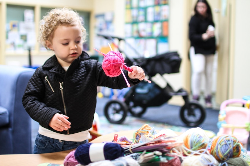 Toddler Holly Pilling picking up a pink ball of wool amongst a pile of donated woollen balls.